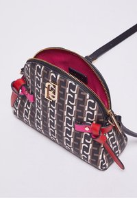 Pieni suunnittelijan olkalaukku, jossa on ruskea ja beige kuvioitu ulkopinta, punaiset ja vaaleanpunaiset nahkakoristeet, kultainen vetoketju ja magentansävyinen sisävuori.