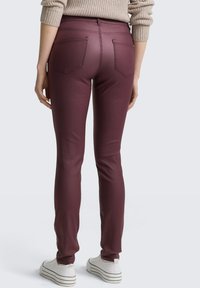 Pantalons ajustés bordeaux fabriqués dans un matériau extensible, avec une texture lisse, deux poches arrière et une taille conçue pour un ajustement serré.