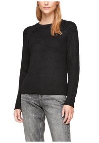 Pull en tricot noir avec une texture côtelée, col rond et manches longues. Associé à un jean texturé gris clair.