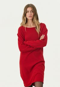 Robe rouge surdimensionnée en tissu doux, avec un col rond et des manches longues, offrant une coupe décontractée et un ourlet légèrement incurvé.