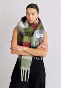 Grote, meerkleurige geruite sjaal in groen, rood, wit en grijs, met franjes aan de uiteinden en een wit label met de tekst "ARCTIC FOX."