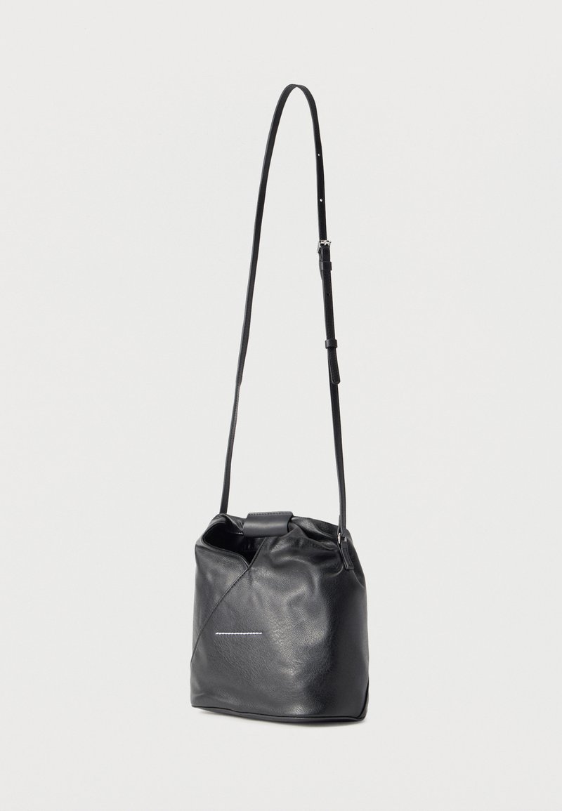 Sac seau en cuir noir avec bandoulière réglable et petit détail blanc cousu à l'avant, présenté sur un fond uni.