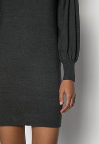 Robe tricotée gris foncé avec des manches longues bouffantes, des poignets et un ourlet côtelés. Le tissu a une texture douce et une silhouette ajustée.