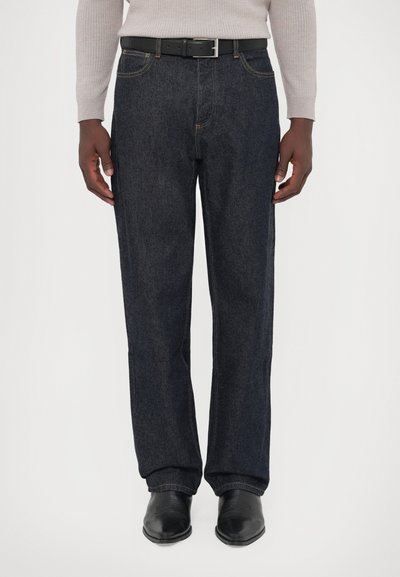 Tamno plavi traperice s ravnim nogavicama, sličice žute niti, dizajnom s pet džepova i crnim kožnim remenom učvršćenim srebrnom kopčom.