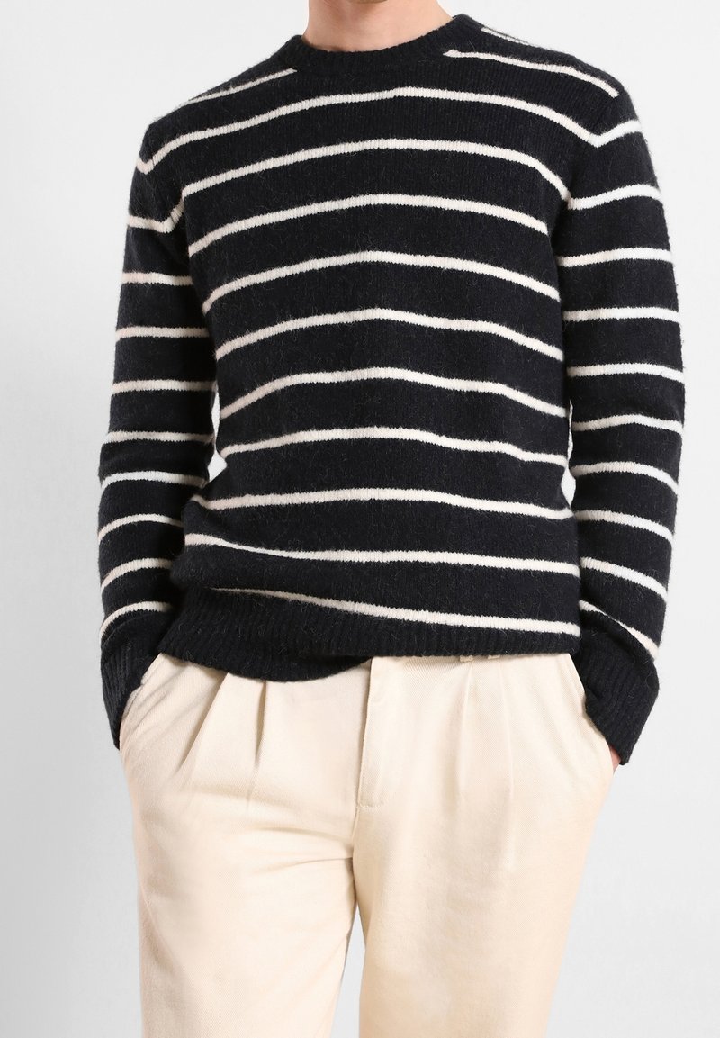 Granatowo-biały sweter w paski wykonany z miękkiego, teksturowanego materiału, z okrągłym dekoltem, w połączeniu z jasnobeżowymi spodniami plisowanymi.