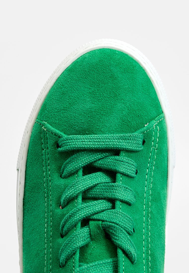 Grüne Wildleder-Sneaker mit weißer Gummisohle, ausgestattet mit passenden grünen Schnürsenkeln, die in einer klassischen Schleife gebunden sind.