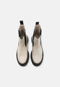 Bottines en cuir beige clair avec des panneaux latéraux élastiques noirs et une semelle noire épaisse. Dotées d'une languette pour faciliter l'enfilage.