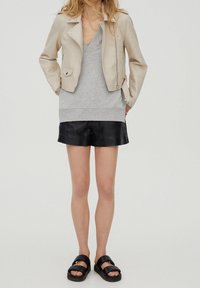 Beige Leder-Motorradjacke, grauer V-Ausschnitt-Pullover, schwarze Leder-Shorts und schwarze Sandalen mit breiten Riemen. Einfaches, modernes Design.