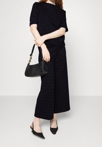 Top a scacchi blu navy e pantaloni a gamba larga realizzati in tessuto textured; abbinati a una borsa nera con effetto coccodrillo e scarpe nere con punta.