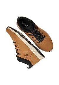 Tan leren sneakers met zwarte accenten, gewatteerde kraag en een getextureerde buitenzool. Voorzien van contrasterende veters en Timberland logo detail.