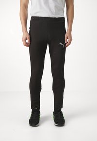Zwarte sportieve broek met elastische tailleband, ritszakken aan de zijkant, taps toelopende pasvorm en Puma-logo in grijs op de linker bovenbeen.