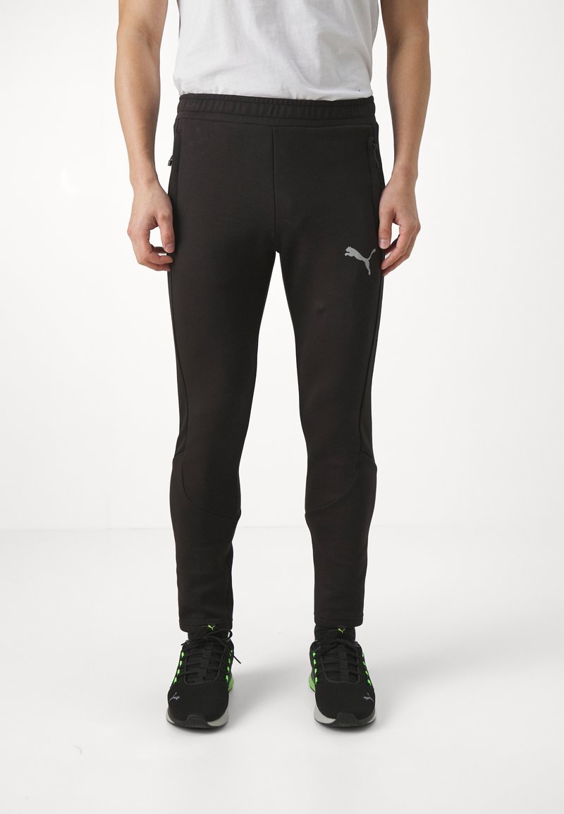 Zwarte sportieve broek met elastische tailleband, ritszakken aan de zijkant, taps toelopende pasvorm en Puma-logo in grijs op de linker bovenbeen.