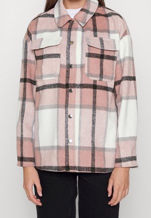 Person wearing a pink, white, and black plaid button-up wool jacket with two chest pockets and black pants against a plain background.