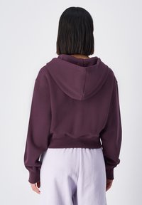 Felpa cropped viola con un ampio cappuccio, polsini a coste e una vestibilità rilassata. Tessuto in cotone misto liscio, dettagli minimal e senza stampe.