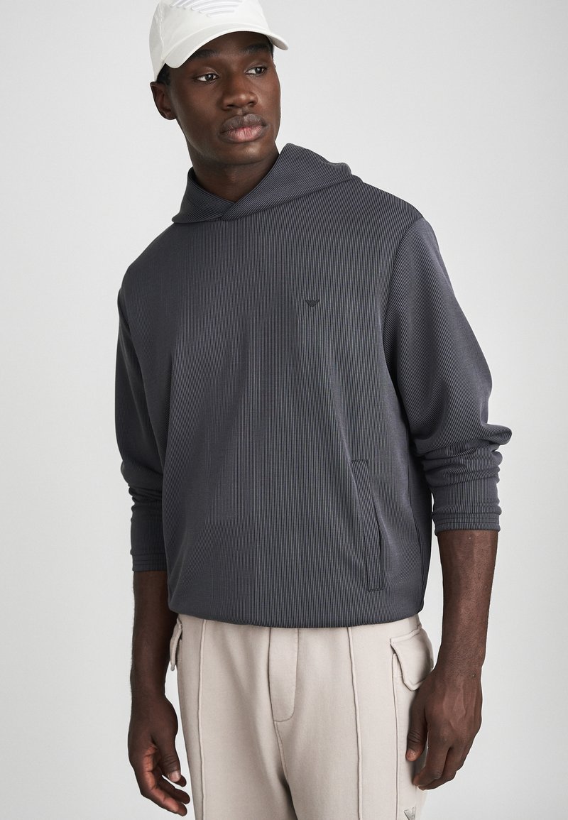 Mørkegrå stripet hettegenser med snøring, frontlomme og ribbede mansjetter, paret med lysebeige bukser. Caps i hvit.