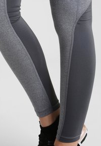 Harmaat urheiluleggingsit, joissa on sileä pinta, tiukka malli ja erottuvat tummat sivupaneelit, täydentäen tyylikästä ilmettä.