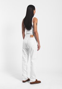 Vaqueros de denim blanco con un corte relajado, presentando una etiqueta de cuero en la parte trasera de la cinturilla, y combinados con una sencilla camiseta sin mangas blanca.