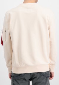 Cremfarbener Pullover mit klassischem Rundhalsausschnitt, gerippten Bündchen und Saum. Verfügt über eine Seitentasche und ein angenähtes Etikett.
