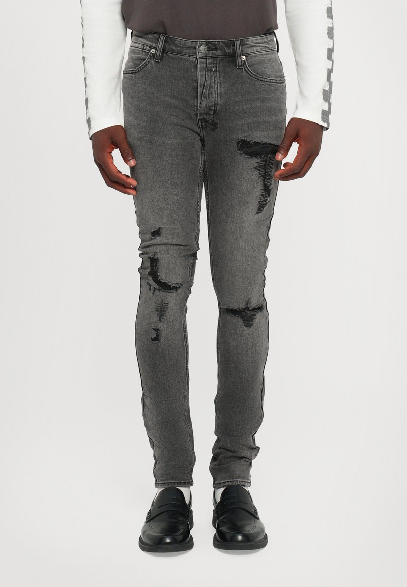 Graue Skinny-Jeans mit distressed Details, mittelhoher Taillenbund, fünf Taschen und minimaler Ausbleichung, kombiniert mit schwarzen Schuhen.