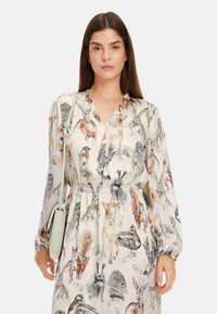 Langärmliges, cremefarbenes Kleid mit einem Allover-Druck verschiedener Tiere in detaillierten Skizzen, einem elastischen Taillenbund und einem V-Ausschnitt.