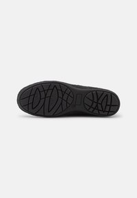 Suela de calzado negra con una superficie de goma texturizada, que presenta un patrón de banda de rodadura con formas circulares y ovaladas para proporcionar agarre y tracción.