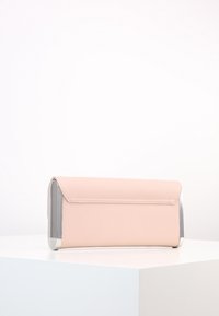 Růžové obdélníkové psaníčko s kovovými stříbrnými okraji, ležící na bílém povrchu proti jednotnému bílému pozadí.