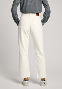 Vita vida byxor med hög midja, två bakfickor och en läderlapp på midjebandet. Bärs med en grå långärmad skjorta.