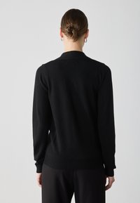 Maglione nero a maglia con maniche lunghe, polsini e orlo a costine, e colletto classico. Texture liscia, design aderente, dettagli minimi.