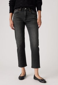 Blugi negri din denim cu croială dreaptă, talie înaltă, cinci buzunare și un efect subtil de decolorare, asortați cu pantofi negri cu talpă plată.