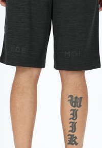 Donkergrijze sportshorts van een gestructureerde stof, met subtiele branding op de zoom. Zichtbare been tatoeage met een opvallend tekstontwerp.