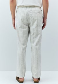 Pantalon de couleur claire avec une texture et un motif à rayures verticales, doté d'une coupe décontractée et d'une taille élastique, conçu pour le confort.