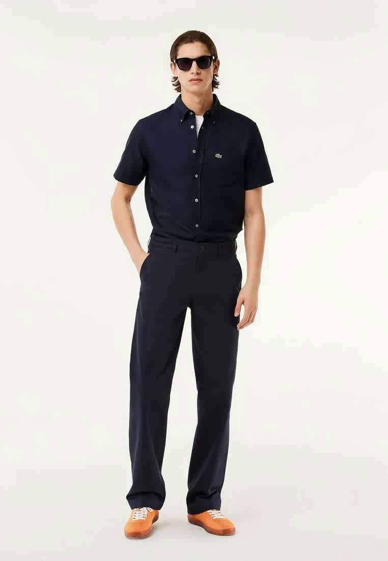 Chemise bleu marine à manches courtes avec un petit logo, associée à un pantalon bleu marine foncé et des baskets orange sur un fond uni.