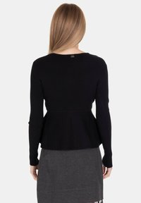 Maglietta nera a maniche lunghe con design a peplum, caratterizzata da un collo rotondo e un'etichetta con marchio discreta sul retro.