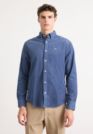 Blaues Hemd mit Knopfleiste aus strukturiertem Stoff, das über einen klassischen Kragen und lange Ärmel verfügt. Auffälliges gesticktes Logo auf der Brust.