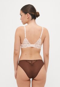 Reggiseno con coppe a balconcino in pizzo rosa chiaro con spalline regolabili; mutandine a vita alta trasparenti marroni con dettagli in pizzo floreale sul retro.