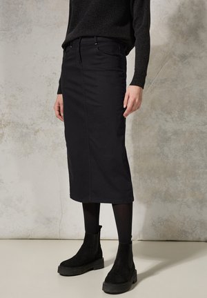 Schwarzer Baumwollmischung Midi-Rock mit geradem Schnitt, Fronttaschen und subtilen Nähten, kombiniert mit schwarzen Stiefeletten und Strumpfhose.