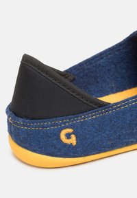 Pantofole in feltro blu navy con rifiniture in tessuto nero, suola in gomma gialla e dettagli cuciti. Accento del logo arancione ben visibile sul lato.