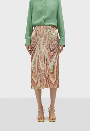 Pailletten midi-rok met een golfpatroon in tinten roze, groen en goud, gecombineerd met een groen blouse met lange mouwen en gele hakken.