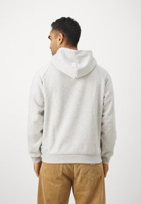 Felpa grigia con cappuccio realizzata in tessuto morbido, con una vestibilità comoda, polsini a coste e tasca a marsupio. Indossata con pantaloni in velluto a coste beige.