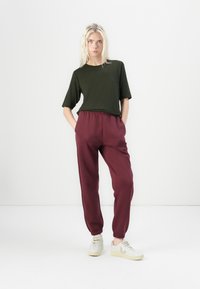 Tmavě zelené zkrácené tričko s kulatým výstřihem, doplněné burgundskými zúženými tepláky s elastickým pasem a manžetami. Bílé tenisky.