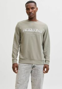 Olivengrøn sweatshirt med rund hals og ribbede ærmer. Har hvid "JACK&JONES"-logo foran og tekstureret stof. Kombineret med lyse jeans.