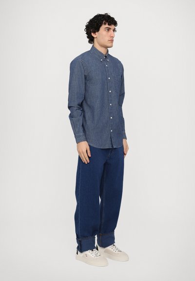 Camicia in denim leggera di colore blu scuro, con colletto a bottoni e maniche lunghe. Abbinata a jeans blu a vita alta e sneakers crema.