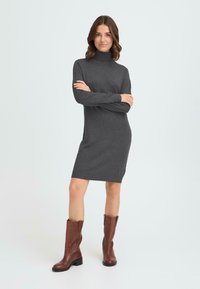 Siva, dugi rukav, turtleneck haljina s uskim siluetom, pletenom teksturom i logotipom blizu donjeg ruba. Nosena s smeškastim čizmama do koljena.