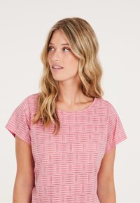 Camisa de manga corta rosa con un patrón geométrico de líneas y puntos pequeños. Tejido suave, ajuste relajado, escote redondo y textura lisa.