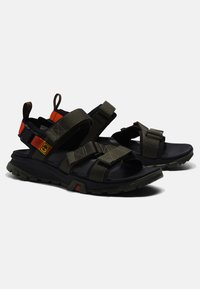 Dark green sandals with adjustable straps, rubber soles, and orange accents; features textured material and a rugged design for traction.