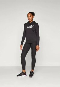 Μαύρη μπλούζα φούτερ με λευκό λογότυπο "PUMA", συνδυασμένη με μαύρα κολάν και μαύρα αθλητικά παπούτσια. Απαλή ύφανση, εφαρμοστή σχεδίαση και αθλητική εμφάνιση.