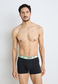 Schwarze Nike Boxershorts mit einem hellgrünen Bund, der das Nike-Logo trägt, aus einem glatten, dehnbaren Material gefertigt.