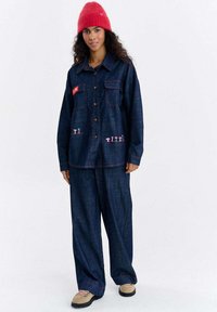 Zestaw kurtka jeansowa i spodnie w ciemnoniebieskim kolorze z różowym przeszyciem. Z dwoma kieszeniami na piersi i wyszywanymi wzorami grzybów na przednich kieszeniach.