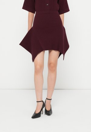 Robe en tricot côtelé bordeaux avec des manches courtes, ourlet asymétrique, texture du tissu, associée à des chaussures à talons hauts noires avec une bride au niveau de la cheville.