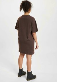 Brązowa bawełniana sukienka T-shirt z luźnym krojem, krótkimi rękawami, bocznymi rozcięciami i okrągłym dekoltem, zestawiona z czarnymi sznurowanymi botkami za kostkę.